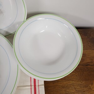 May include: A set of white ceramic bowls with a green and blue rim. The bowls are stacked on top of each other.