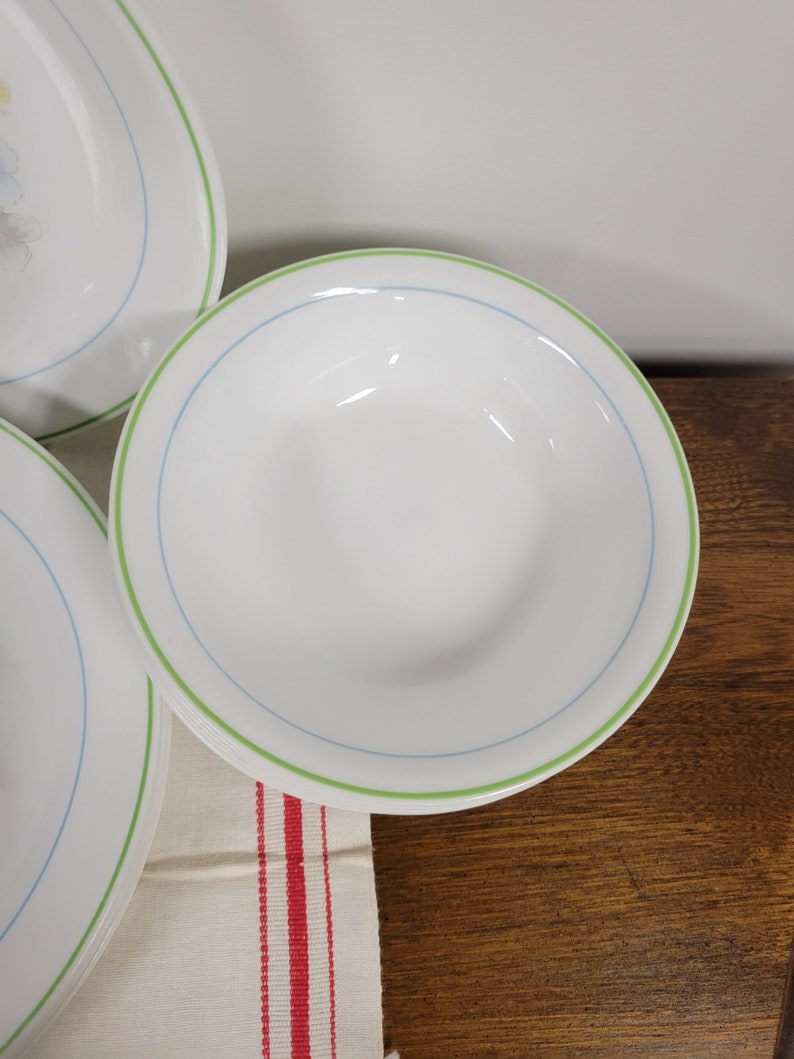 May include: A set of white ceramic bowls with a green and blue rim. The bowls are stacked on top of each other.