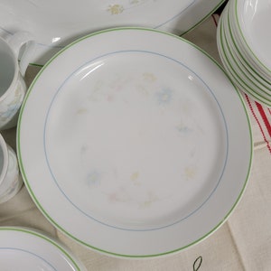 May include: A set of white ceramic dinnerware with a green and blue floral pattern. The plates have a green rim and a blue floral design in the center.