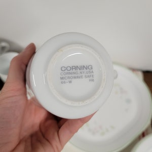 May include: White ceramic mug with the text "CORNING CORNING, NY, USA MICROWAVE SAFE 66-W H6" on the bottom.