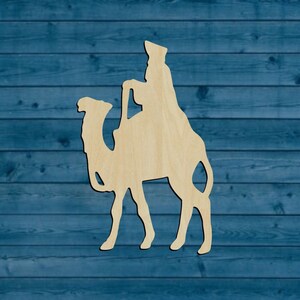 May include: Wooden cutout of a person riding a camel. The cutout is a light brown color and is perfect for crafting projects.