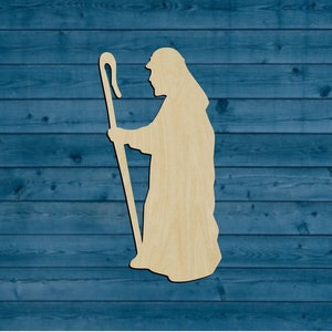 May include: Wooden cutout of a shepherd holding a staff with a curved top. The cutout is a light brown color and is set against a blue wooden background.