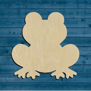 May include: A wooden cutout of a frog in a light brown color. The frog is sitting on a blue wooden background.