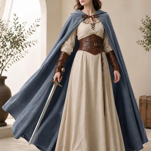 May include: A floor-length beige dress with long sleeves and a lace-up neckline, paired with a blue hooded cloak, a brown leather corset belt, and matching brown leather arm bracers. A metal sword with a cross-guard is held in one hand.