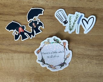 May include: A collection of stickers with a witch theme. The stickers include illustrations of witches with umbrellas, a salt shaker, sprigs of lavender, a heart, and a sticker with the text "There's a little witch in all of us."