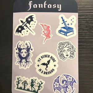 Puede incluir: Una hoja de pegatinas de temática fantástica con varios diseños. Incluye un murciélago con una espada, un hada, una espada y libros, una mujer con cuernos, una Medusa, un dragón y el texto "My Other Ride Is A Dragon". La palabra "fantasy" está en la parte superior.
