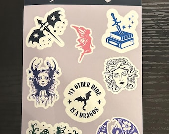 May include: A sheet of fantasy-themed stickers featuring various designs. Included are a bat with a sword, a fairy, a sword and books, a woman with antlers, a Medusa, a dragon, and the text "My Other Ride Is A Dragon". The word "fantasy" is at the top.