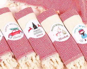 May include: Six red and white Turkish towels with festive Christmas designs and names, rolled up and tied with a white ribbon. The towels are in a wicker basket.
