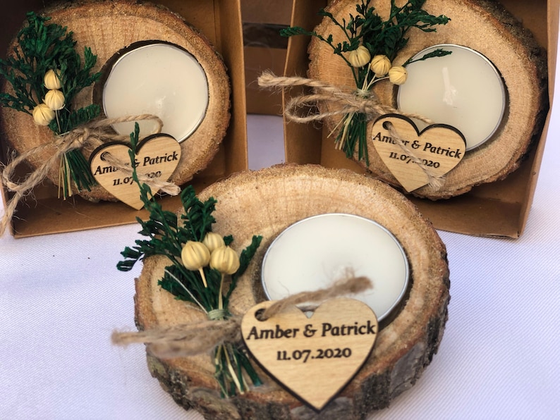 May include: Wooden candle holders with a small white tea light candle in each. Each holder has a small heart-shaped tag with the text "Amber & Patrick 11.07.2020" and a small bouquet of dried flowers.