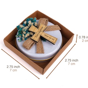 May include: A baptism favor in a brown box, measuring 2.75 inches (7 cm) square and 0.78 inches (2 cm) high. It features a wooden cross with the text "Tom's Baptism" and the date "25.07.2025", along with blue and white flowers.