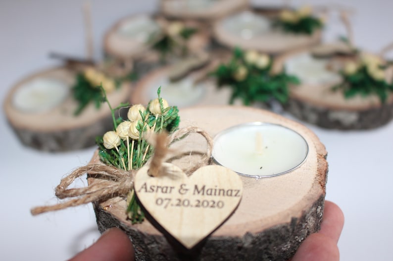 May include: Wooden candle holder with a heart-shaped tag that says "Asrar & Mainaz 07.20.2020". The holder is decorated with greenery and small white flowers.