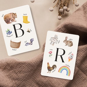 May include: Two white cards with colorful illustrations and the letters B and R. The B card shows a bear, boots, blueberries, a bee, a basket, and a bat. The R card shows a robot, a rabbit, a rose, a rocket, a rooster, and a rainbow.