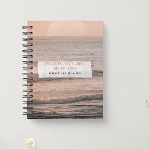 Op de afbeelding: Een spiraalgebonden notitieboek met een zonsondergang boven de oceaan op de omslag. De tekst op de omslag luidt "The storm, the silence, and the voice. Reflections from Job."