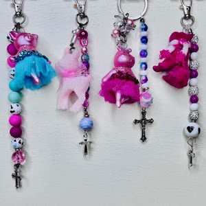 May include: A selection of keyrings with decorative charms, including animal figures and crosses. The keyrings feature colourful beads in shades of pink, blue, and white. Each keyring has a silver-tone clasp.
