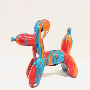 May include: A colorful balloon dog sculpture with a glossy finish. The sculpture features a vibrant mix of red, orange, and blue paint drips. The dog is posed in a playful stance, adding a touch of whimsy to any space.