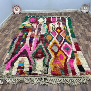 May include: A colorful Moroccan rug with a geometric pattern in shades of pink, red, green, and yellow. The rug has a fringe border and is made of wool.