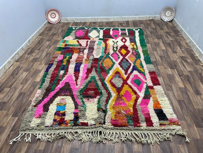 May include: A colorful Moroccan rug with a geometric pattern in shades of pink, red, green, and yellow. The rug has a fringe border and is made of wool.