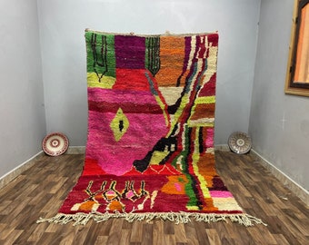 May include: A colorful Moroccan rug with abstract geometric patterns in shades of pink, red, orange, green, and yellow. The rug has a fringe border and is woven with a variety of textures.
