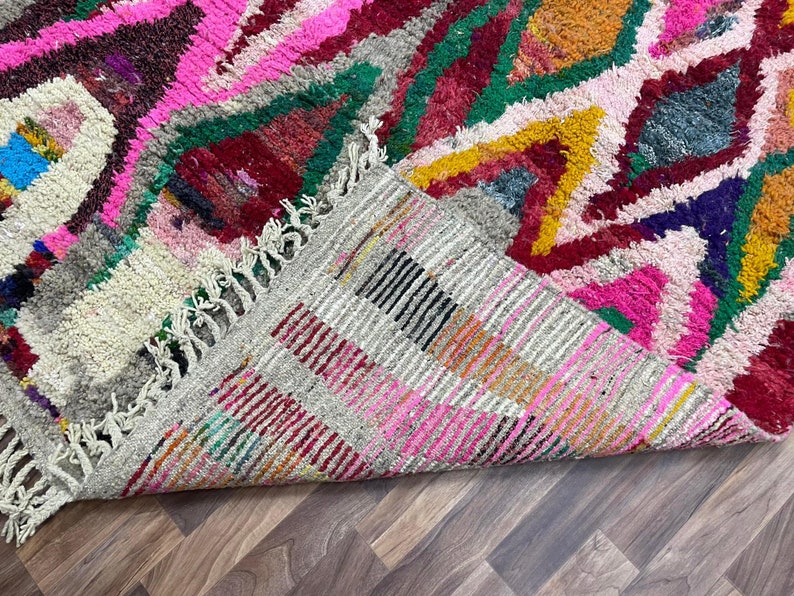 May include: A colorful Moroccan rug with a geometric pattern in shades of pink, red, green, yellow, and blue. The rug has a fringe border and is folded in half.