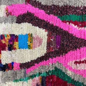 May include: A colorful Moroccan rug with a pink, green, and red geometric pattern. The rug is made of wool and has a soft, fluffy texture.