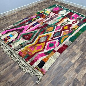 May include: A colorful Moroccan rug with a geometric pattern in shades of pink, green, yellow, and red. The rug has a fringe border and is woven with a variety of textures.