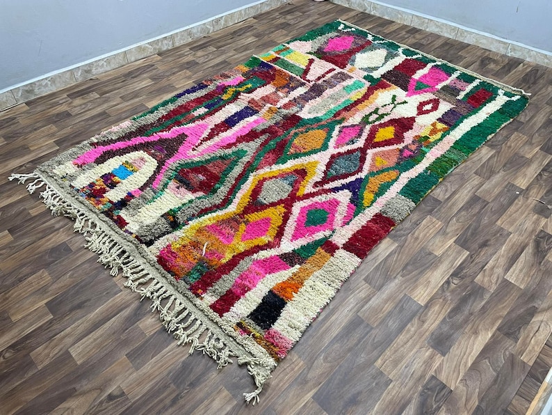 May include: A colorful Moroccan rug with a geometric pattern in shades of pink, green, yellow, and red. The rug has a fringe border and is woven with a variety of textures.