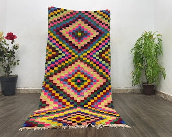 May include: A colorful Moroccan rug with a geometric pattern of squares and diamonds in shades of pink, yellow, green, blue, red, and black.