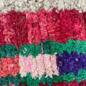 May include: Close-up of a colorful, textured rug with stripes of red, pink, green, and purple. The rug is made of woven wool and has a fuzzy texture.