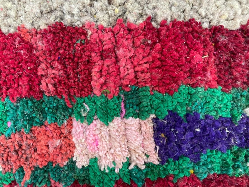 May include: Close-up of a colorful, textured rug with stripes of red, pink, green, and purple. The rug is made of woven wool and has a fuzzy texture.