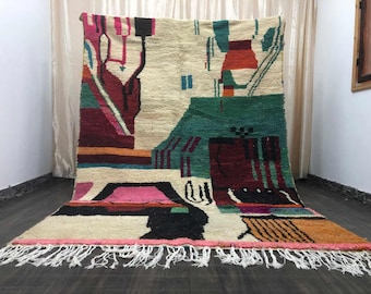Puede incluir: Una alfombra rectangular grande con un diseño abstracto. La alfombra presenta un fondo color crema con formas geométricas coloridas en tonos de rosa, verde, rojo y negro. La alfombra tiene flecos a lo largo del borde inferior.