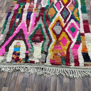 May include: A colorful Moroccan rug with a geometric pattern in shades of pink, green, yellow, and red. The rug has a fringe border.