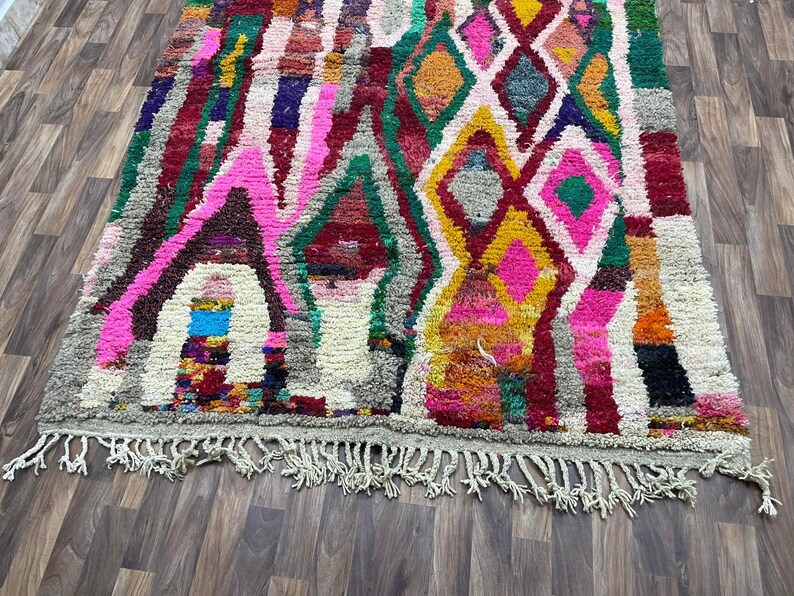 May include: A colorful Moroccan rug with a geometric pattern in shades of pink, green, yellow, and red. The rug has a fringe border.