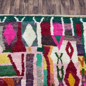 May include: A colorful Moroccan rug with geometric patterns in shades of pink, red, green, white, and yellow. The rug has a fringe border.