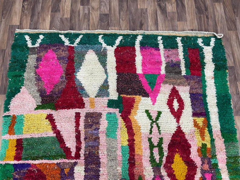 May include: A colorful Moroccan rug with geometric patterns in shades of pink, red, green, white, and yellow. The rug has a fringe border.