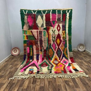 May include: A colorful Moroccan rug with a geometric pattern in shades of pink, red, green, yellow, and blue. The rug has a fringe border and is woven with a variety of textures.