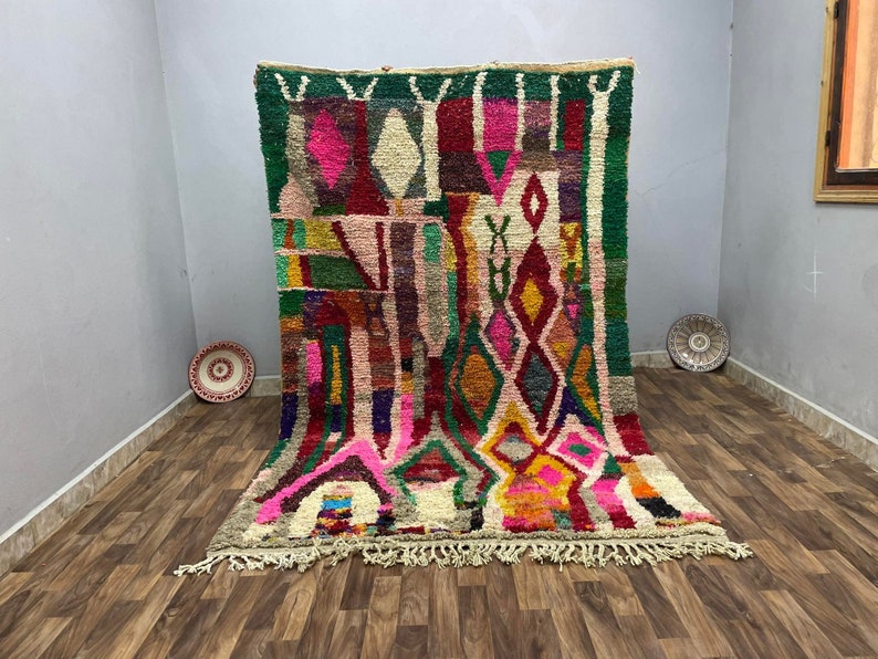May include: A colorful Moroccan rug with a geometric pattern in shades of pink, red, green, yellow, and blue. The rug has a fringe border and is woven with a variety of textures.