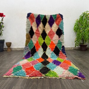 May include: A colourful Moroccan rug with a diamond pattern in shades of pink, green, blue, black, and white. The rug is made of wool and has a hand-woven texture.