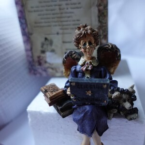 Könnte beinhalten: Eine Figur einer Frau mit Engelsflügeln, die eine Brille und ein blaues Kleid trägt, hält ein Buch mit der Aufschrift "Get Smart" und "Computing". Sie hat Flügel und sitzt auf einer weißen Oberfläche mit einer kleinen Hundefigur neben ihr.