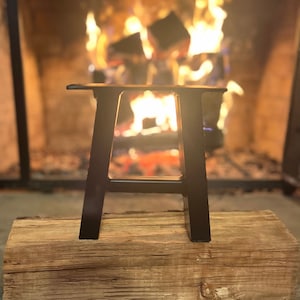Pode incluir: Pernas de mesa em A de metal preto, sentadas em um tronco de madeira na frente de uma lareira com fogo.