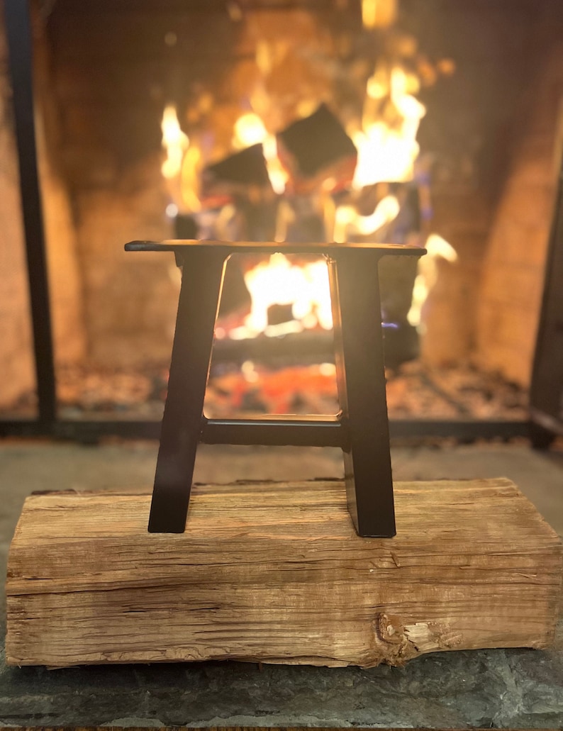Pode incluir: Pernas de mesa em A de metal preto, sentadas em um tronco de madeira na frente de uma lareira com fogo.