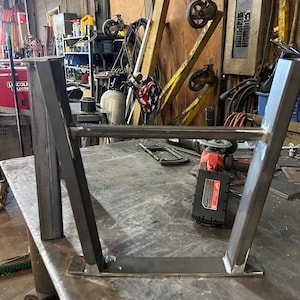 Pode incluir: Uma estrutura de metal com quatro pernas, soldada. A estrutura est&aacute; sentada sobre uma superf&iacute;cie de metal. Uma ferramenta el&eacute;trica &eacute; vis&iacute;vel em primeiro plano.
