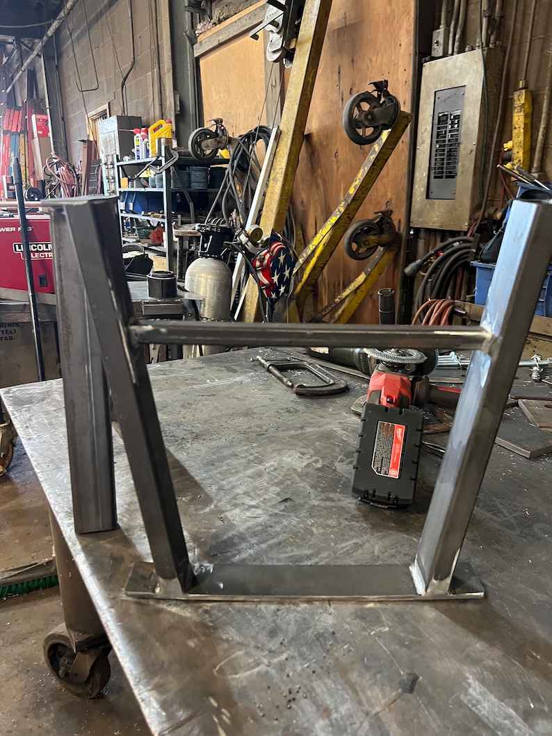 Pode incluir: Uma estrutura de metal com quatro pernas, soldada. A estrutura est&aacute; sentada sobre uma superf&iacute;cie de metal. Uma ferramenta el&eacute;trica &eacute; vis&iacute;vel em primeiro plano.