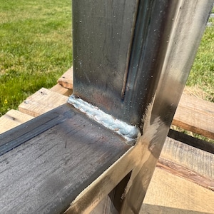 Puede incluir: Primer plano de una uni&oacute;n de metal soldada, que muestra una construcci&oacute;n s&oacute;lida y robusta. El metal es de color gris oscuro y la soldadura es de color gris claro. La soldadura es lisa y uniforme, lo que indica una construcci&oacute;n de alta calidad.