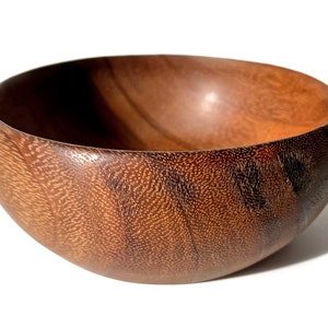 May include: A large, dark brown wooden bowl with a smooth, polished finish. The bowl is made from a single piece of wood and has a natural grain pattern.