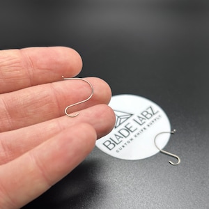 May include: Two silver metal hooks, one held in a hand, the other on a white sticker with the text "BLADE LABZ CUSTOM KNIFE SUPPLY".