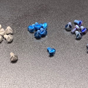 May include: Assortment of small screws with blue and silver finishes. The screws have a triangular head and are arranged in groups on a gray surface.