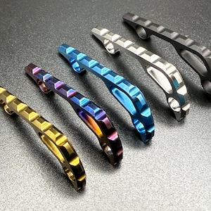 May include: An assortment of colorful bottle openers in gold, iridescent, blue, silver, and black. Each opener has a textured, geometric design and a curved handle with a circular opening.