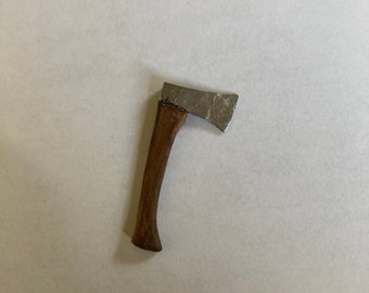Op de afbeelding: Een kleine, zilverkleurige bijl met een houten handvat. De bijl is ongeveer 10 cm lang en heeft een licht gebogen blad.