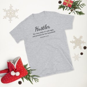 May include: A gray t-shirt with the text "Hustler" in black cursive lettering. The text below reads "She rises while it's still night, and provides for her household Proverbs 31:15".