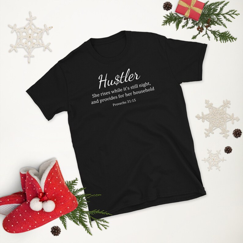 May include: Black t-shirt with white text that reads "Hustler" and a quote from Proverbs 31:15. The quote reads "She rises while it's still night, and provides for her household".